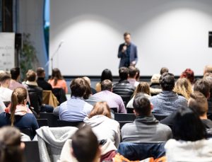 Speaker giving a talk in conference hall at business event. Audience at the conference hall. Business and Entrepreneurship concept. Focus on unrecognizable people in audience.